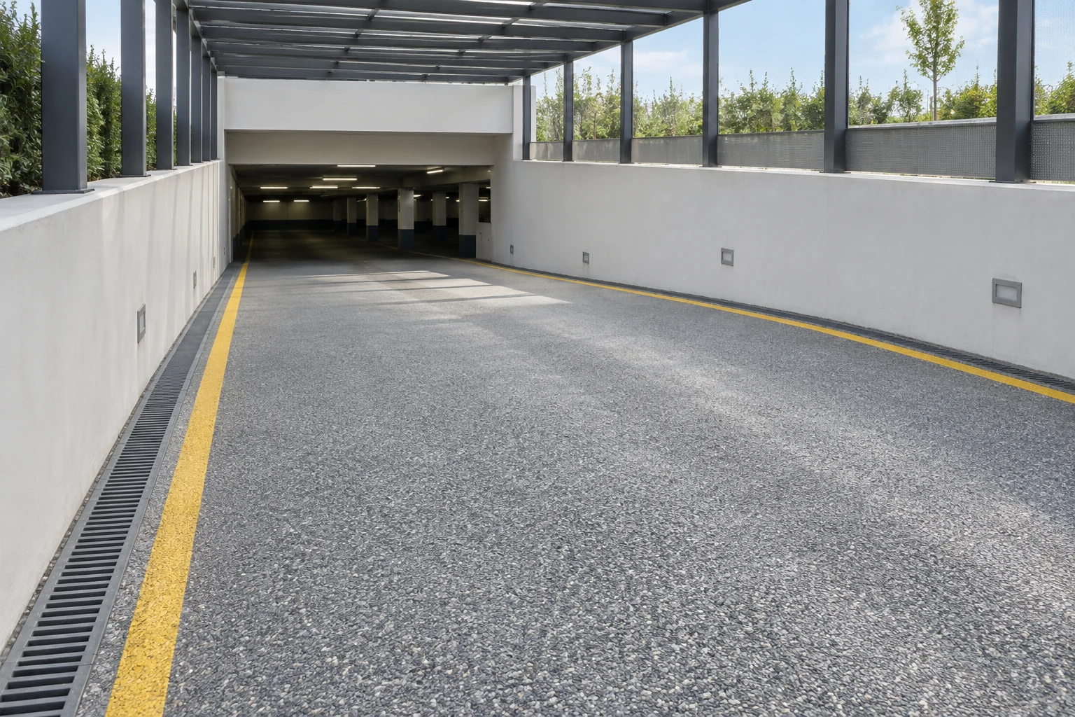 Dokulu gri kaplama, sarı kenar çizgileri ve drenaj kanalı bulunan kapalı otopark giriş rampası